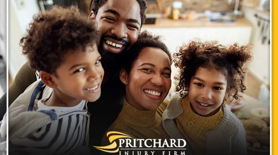 Smiling happy family of four posing indoors with Pritchard Injury Firm logo at the bottom center.