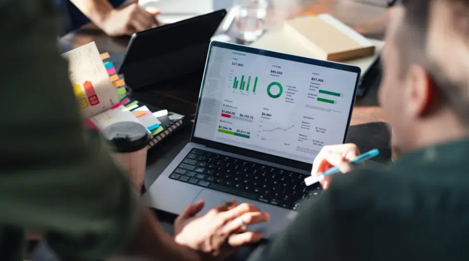People analyzing business data and charts on a laptop during a collaborative meeting at a table.