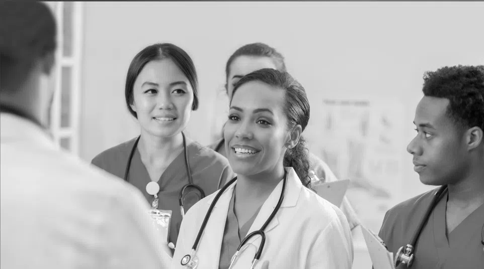 Diverse group of medical professionals discussing patient care in hospital setting, wearing scrubs and stethoscopes.