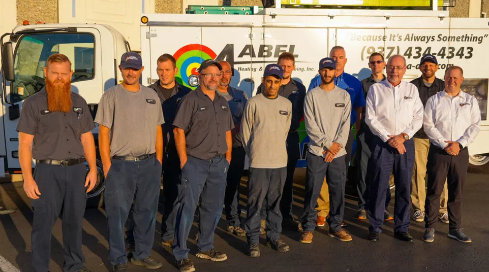 Team of Abel Heating and Cooling employees standing in front of a service truck with company logo in sunlight