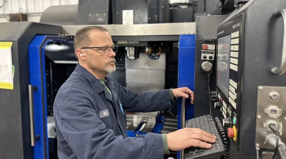 Technician operating a CNC machine, using control panel in a metal fabrication workshop.