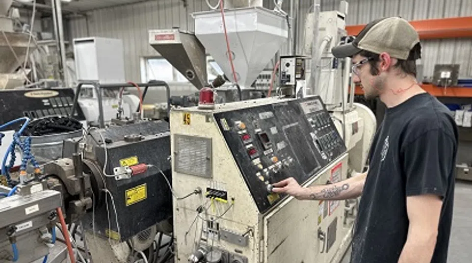 Worker operating industrial injection molding machine in a manufacturing facility with safety glasses and cap