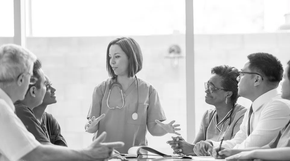 Medical team discussing patient care around conference table with female doctor leading the meeting.