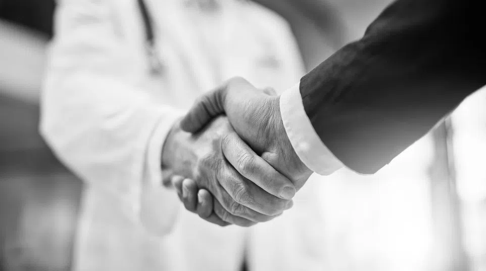 Black and white close-up of a handshake between a doctor and a businessperson symbolizing trust and partnership.