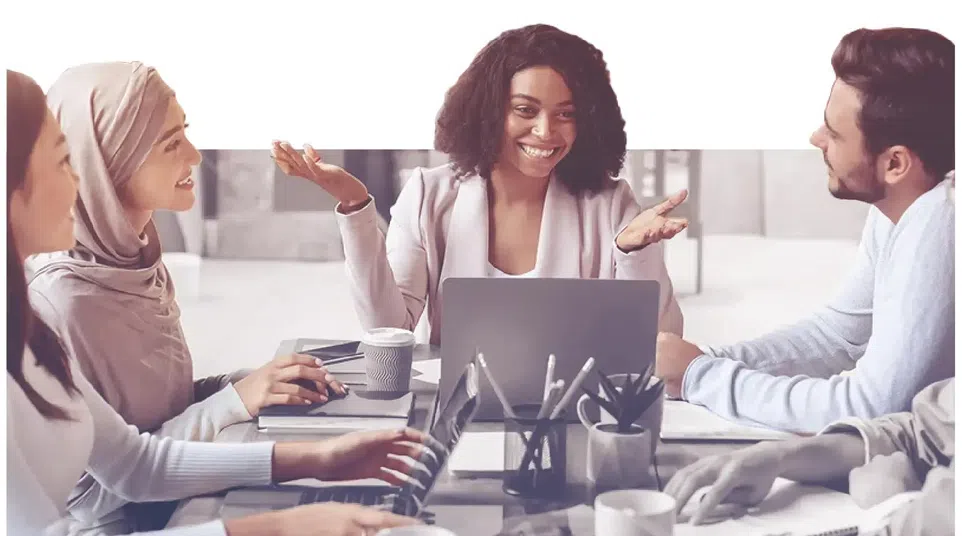 Diverse colleagues collaborating and discussing ideas around a table with laptops and coffee cups in a modern office.