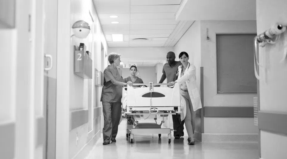 Healthcare professionals transporting a patient on a hospital bed through a corridor, working collaboratively.