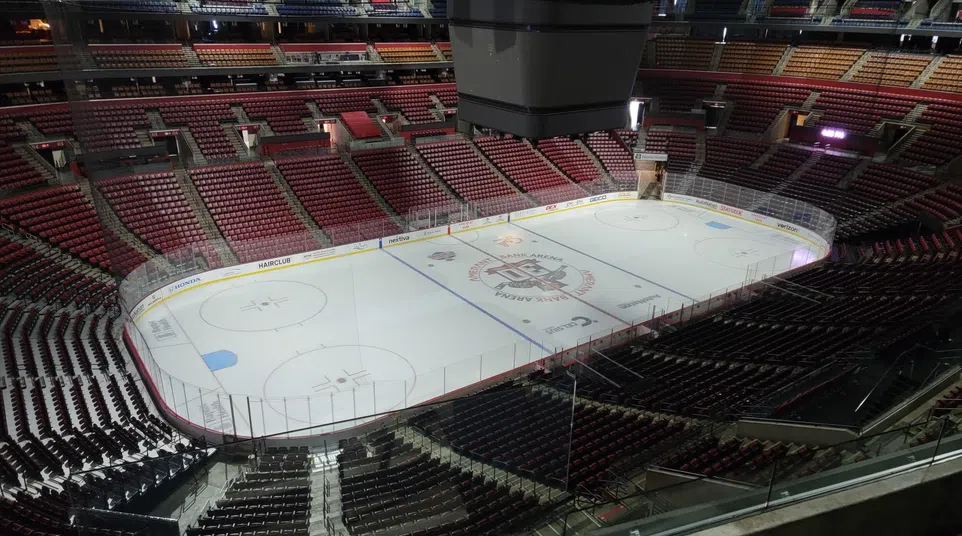 Empty indoor ice hockey arena with ice rink and surrounding red and black seats under bright lights.