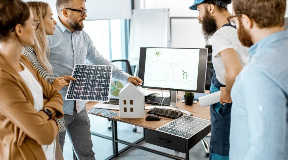 Team discussing solar panel efficiency and renewable energy with solar panels and a home model in office setting.