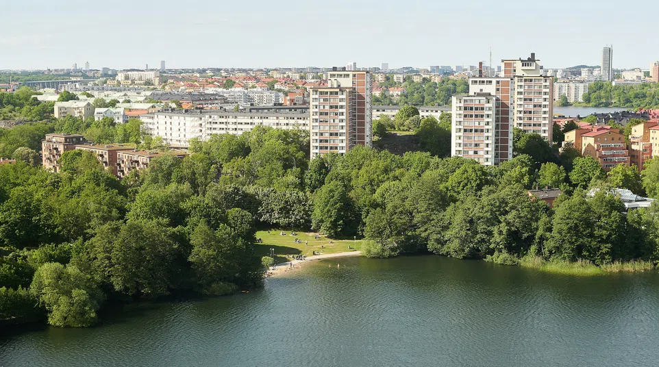 City skyline with residential buildings overlooking a lush green park and a serene lake under blue sky.