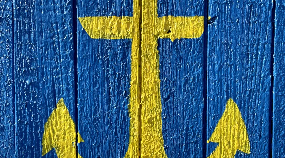 Yellow anchor painted on textured blue wooden planks symbolizing maritime or nautical theme.