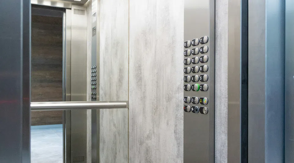 Interior of modern elevator with stainless steel panels, control panel, mirror, and strip ceiling lights.