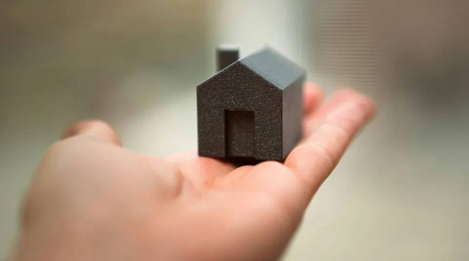 Hand holding a small black house model on blurred background symbolizing real estate or home ownership.