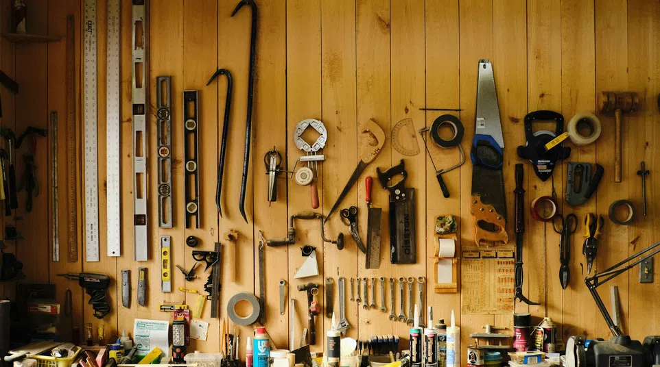 Wooden wall with an assortment of hanging hand tools and measuring instruments in a workshop.