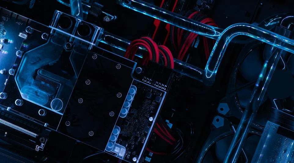 Close-up of a custom PC build featuring water cooling tubes, red cables, and black hardware components under blue lighting.