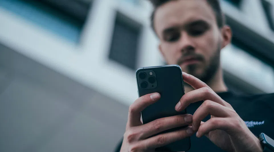 Man using a smartphone outdoors with blurred city buildings in the background.