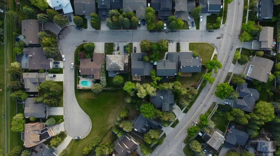 Aerial view of a suburban neighborhood with houses, trees, roads, and a backyard swimming pool.