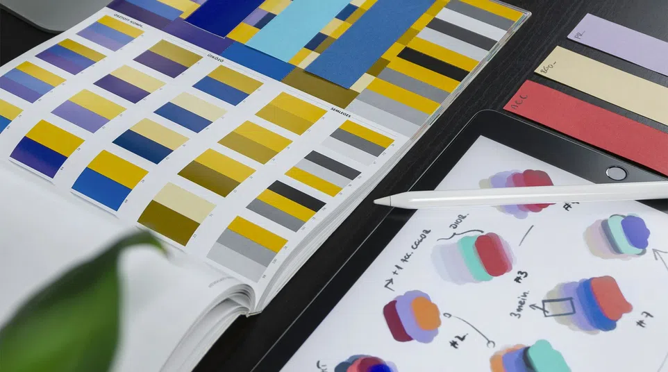 Color swatches, design sketches on tablet, and Apple computer on a creative working desk.