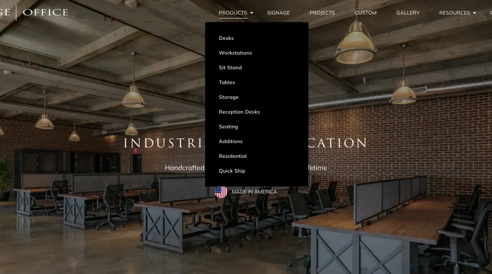 Industrial-style office workspace with wooden desks, black chairs, exposed ceilings, and brick walls under pendant lights