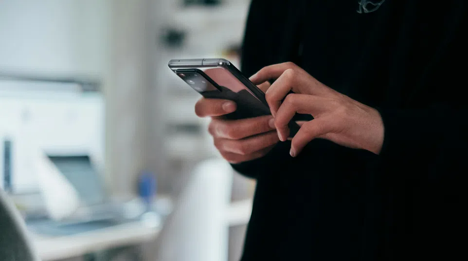 Close-up of person using smartphone indoors with blurred office background, focusing on hands and device interaction.