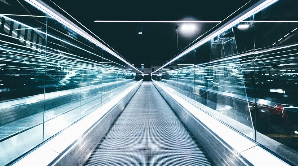 Futuristic illuminated walkway with glass sides and metallic floor in a dark modern setting.