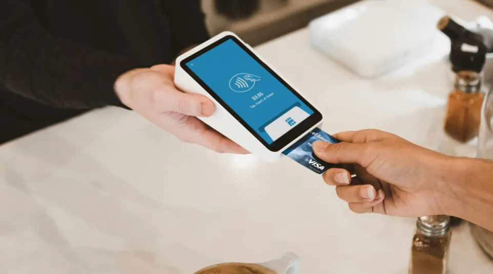 Customer making contactless payment with card at coffee shop counter beside a latte with latte art.