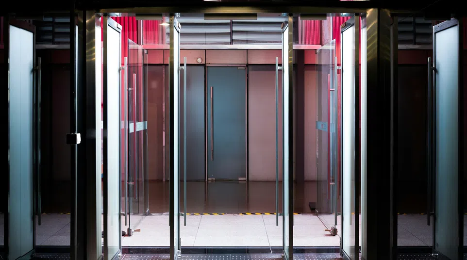 Modern glass revolving door entrance with metal frames and reflections in a dimly lit setting.