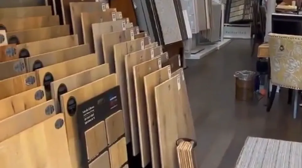 Interior of a flooring showroom with various wood and tile samples displayed on stands and racks under ceiling lights.