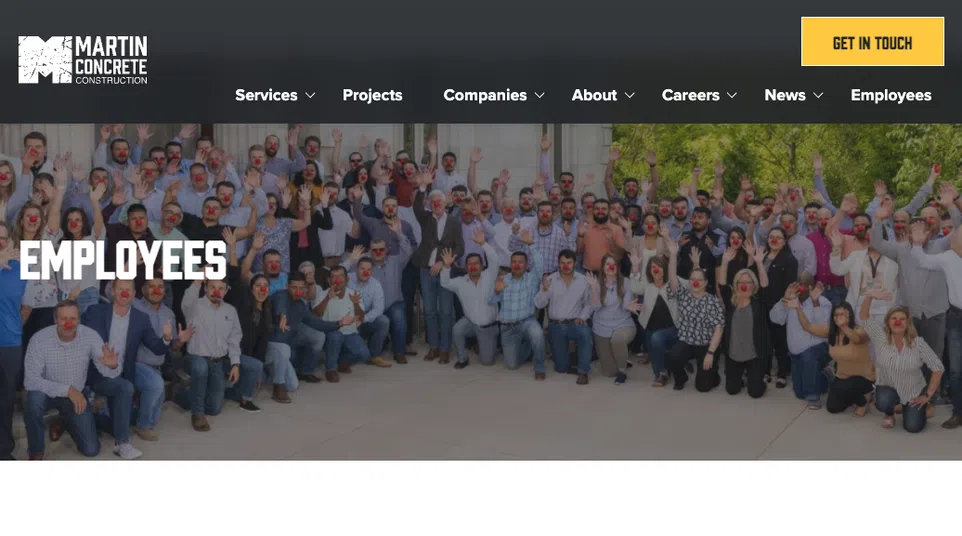 Large group of employees wearing red clown noses posing outdoors in front of Martin Concrete Construction banner.