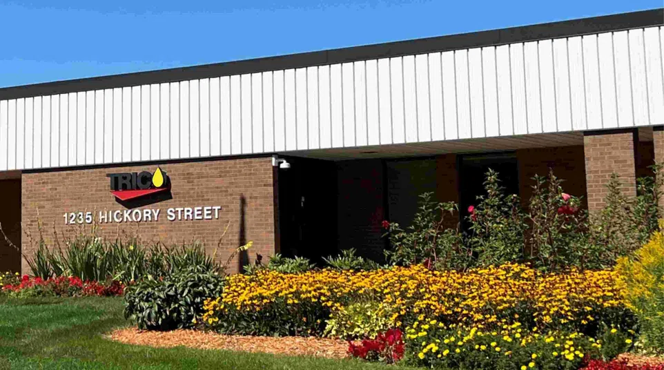 Brick building at 1235 Hickory Street with TRICO sign and vibrant flower beds under clear blue sky
