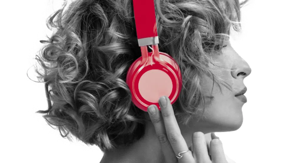 Side profile of a person with curly hair wearing bright red headphones and a light hoodie.