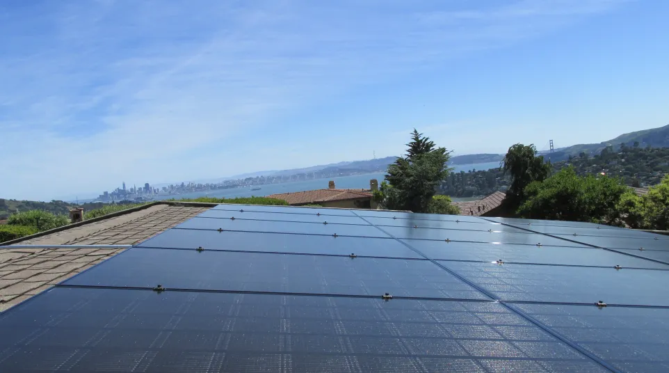 Solar panels installed on a sausalito rooftop with San Francisco skyline and Golden Gate Bridge in the background under blue sky.