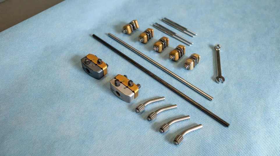 Set of mechanical tools and parts including wrenches, metal rods, clamps, and connectors arranged on blue fabric.