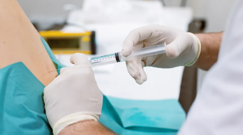 Doctor wearing gloves injecting medication with syringe into patient’s shoulder during treatment.