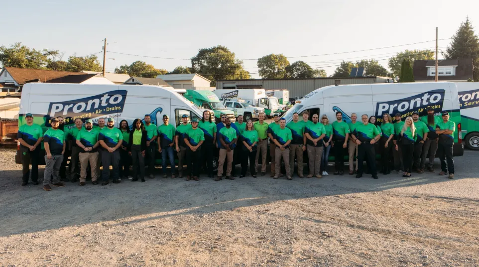 Pronto service team in matching green shirts standing in front of branded service vans at outdoor company lot.