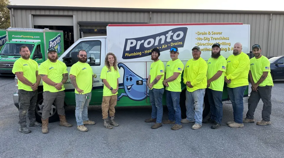 Pronto Plumbing team in neon yellow shirts standing in front of company trucks outside a building at sunset