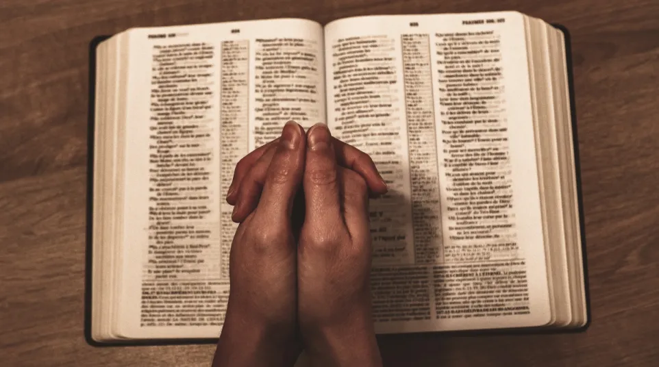 person praying hands with open bible