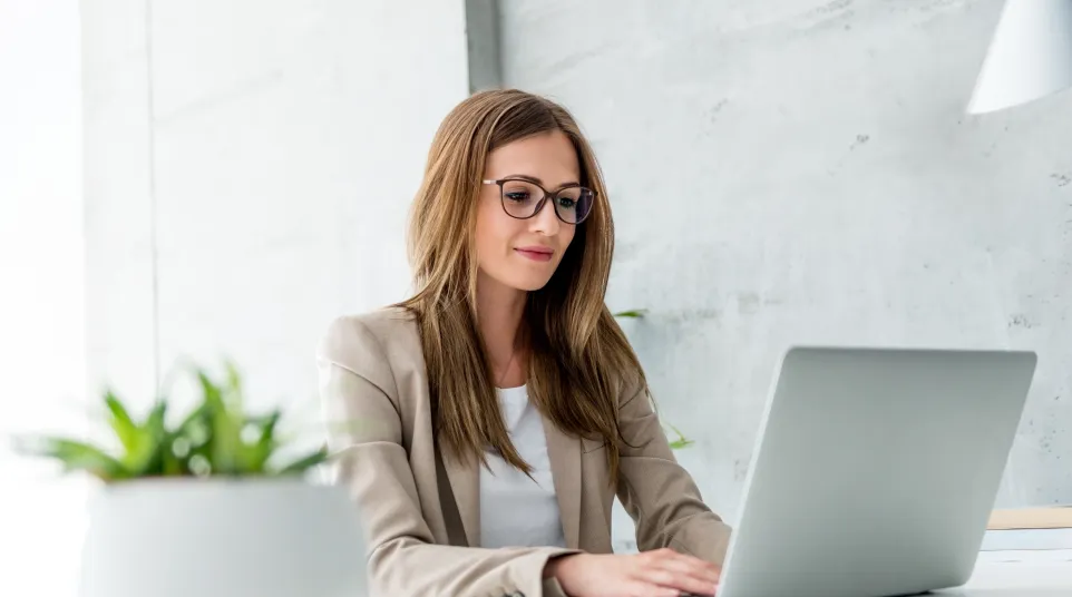Professional woman working on a laptop at a modern office desk with plants.