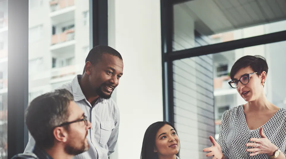 A diverse team collaborates around a laptop in an office setting, discussing ideas and strategies.