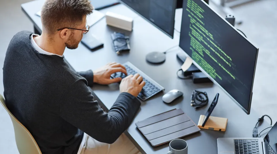 A person coding at a dual-monitor setup with a sleek modern workspace.