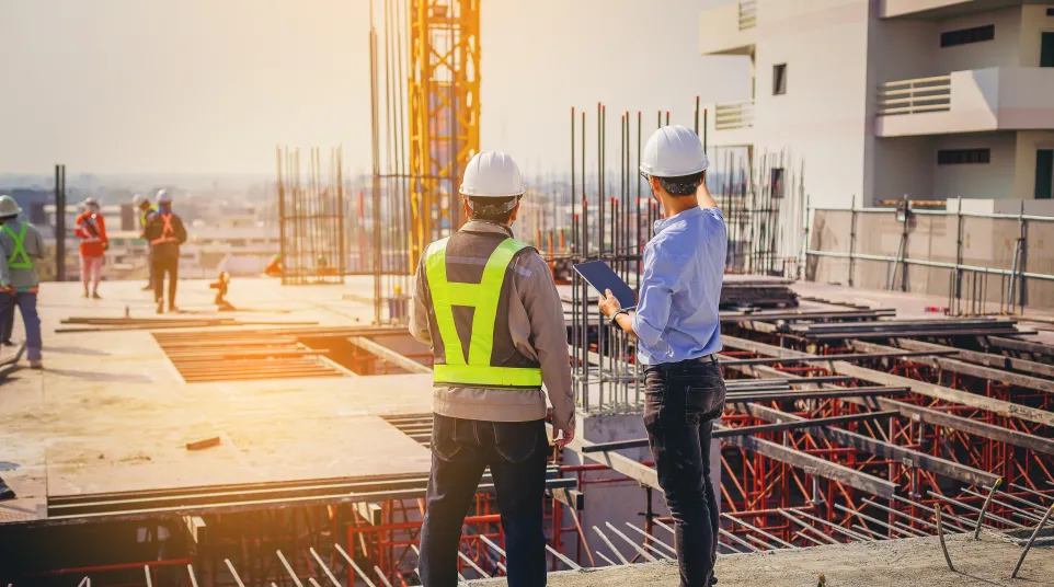Construction workers inspecting a building site during sunset with cranes and scaffolding.