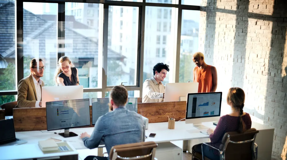 A modern office environment with diverse colleagues collaborating at workstations.