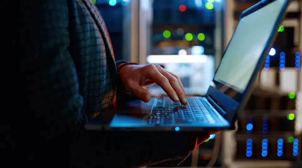 Person using a laptop in a server room with colorful lights in the background.