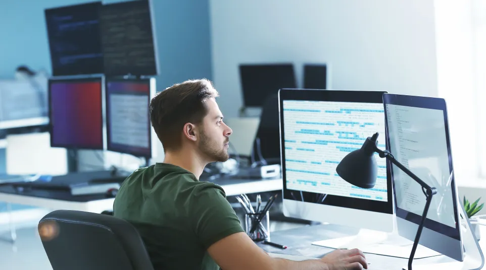 Man working at a dual-monitor workstation in a modern office environment.