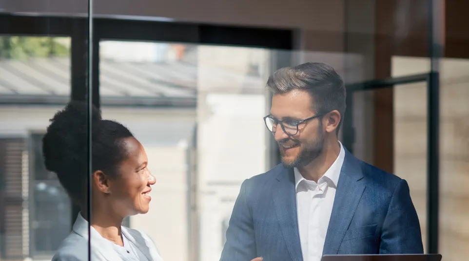 Two professionals discussing in an office space with a laptop and documents, bright and modern environment.