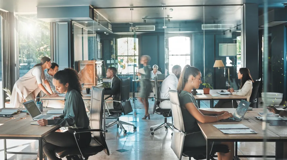 Modern office workspace with diverse professionals collaborating and working on laptops.