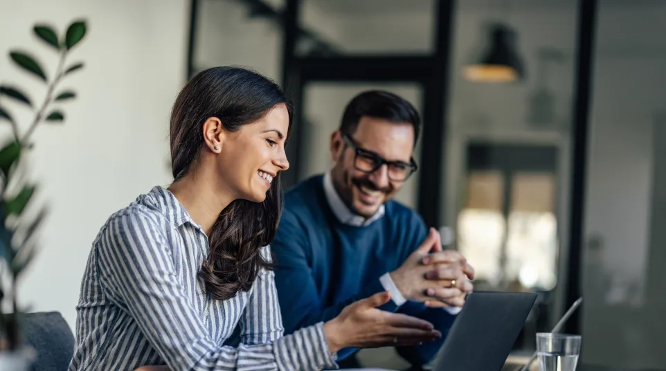 Two professionals engaging in a discussion while working on a laptop in a modern office setting.