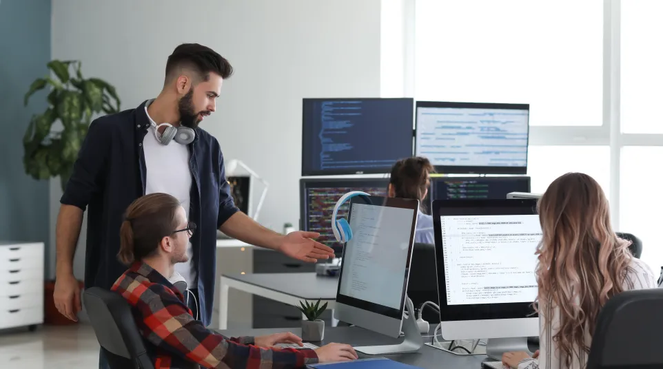 Team of professionals collaborating at modern office workstations with computers and coding on screens.