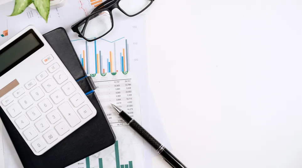 Calculator, glasses, pen, and documents showcasing financial charts and analysis on a white desk.