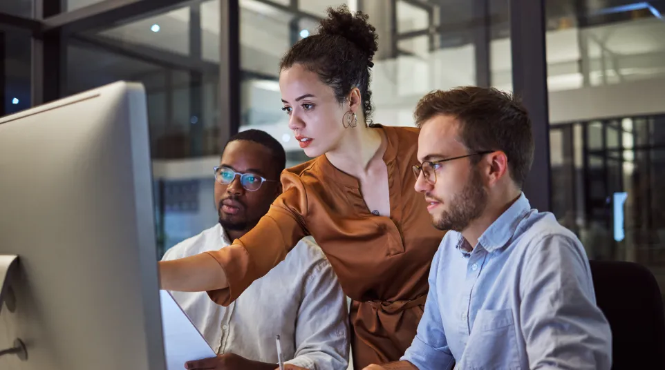 Three colleagues collaborating at a computer in a modern office setting during a work session.