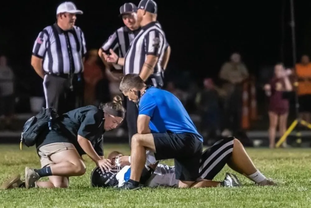Football player receiving medical attention on field with referees and Reid Health Certified Athletic Trainer Kelly McCord nearby at night game